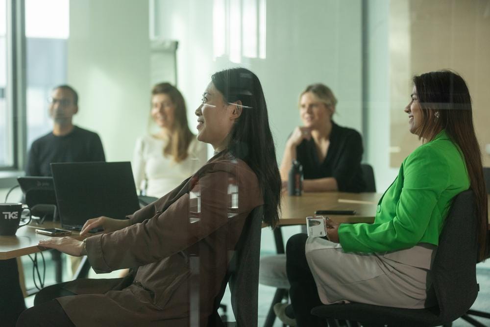 Colleagues smile together around a meeting-room table with laptops.