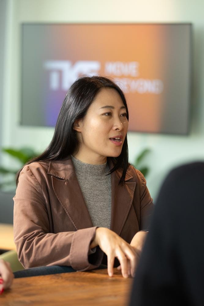 A woman in a blazer speaks at a table in front of a screen showing the TKE “Move Beyond” logo.