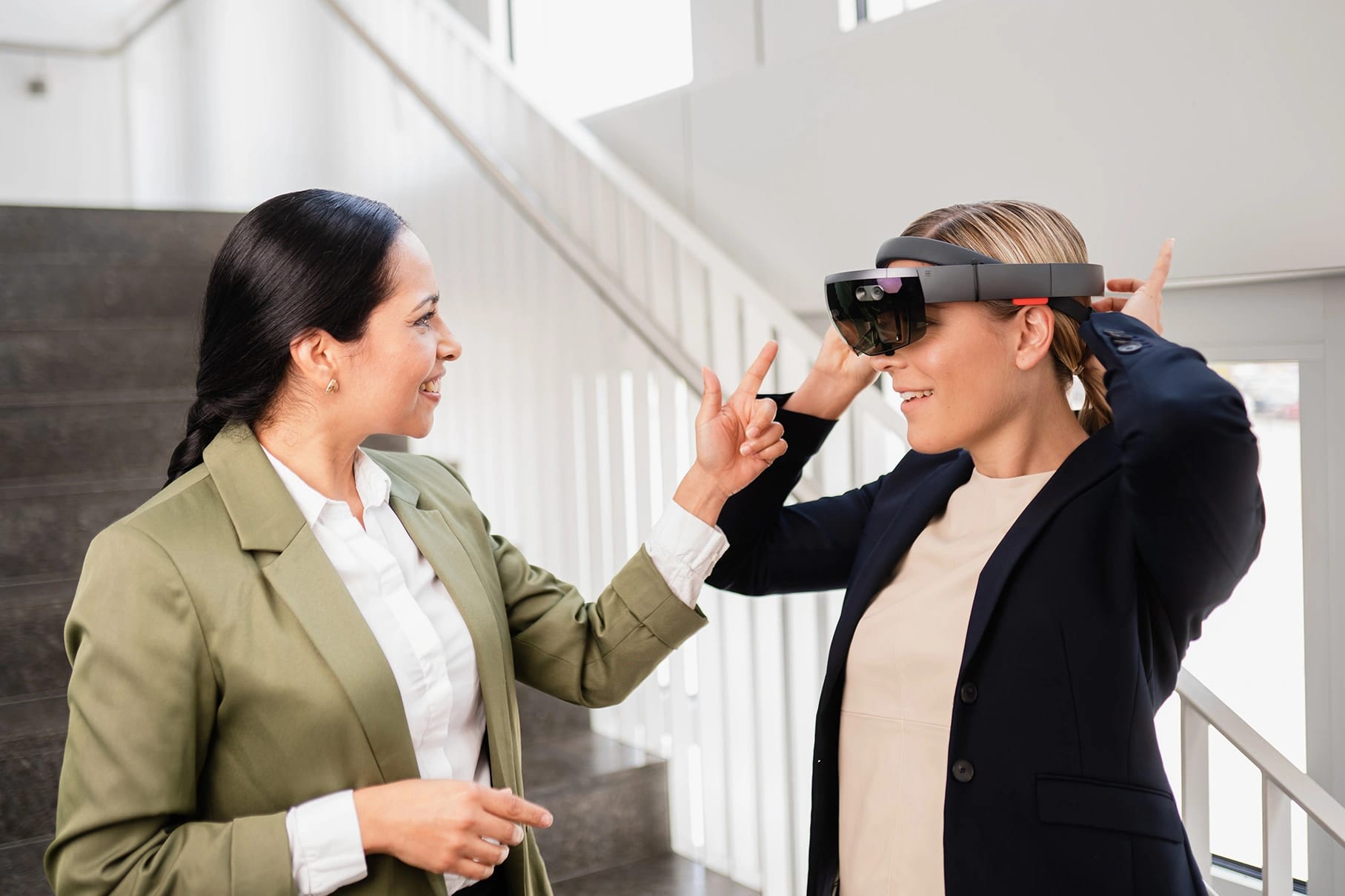 Two colleagues talk on a staircase while one tries on a mixed-reality headset.